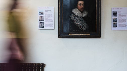A female visitor walks across an exhibition room in front of the portrait of a gentleman.